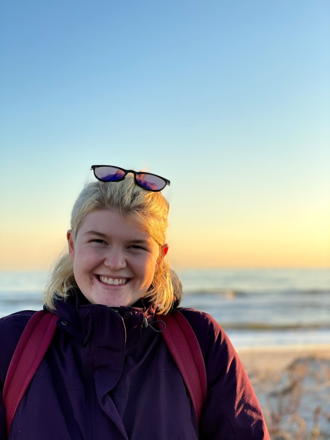 Alexa, in a purple winter coat, stands in front of a beach